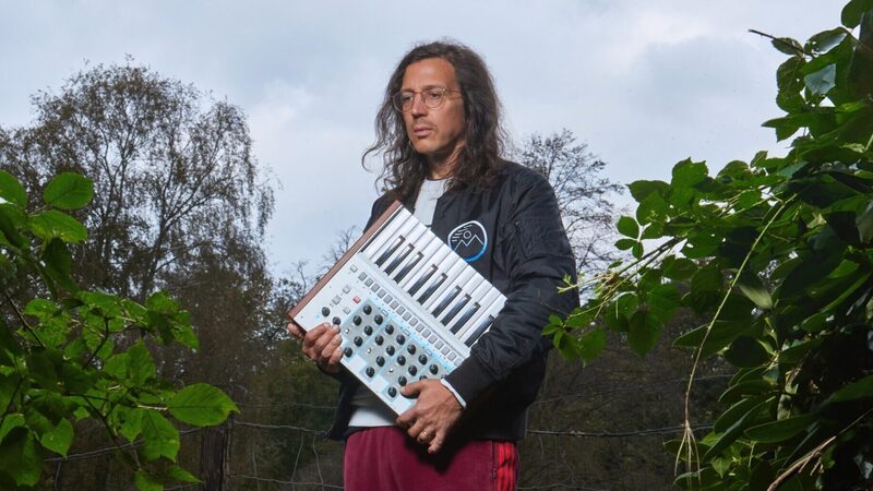 Electro-producer Legowelt in de natuur met een synthesizer onder zijn arm.