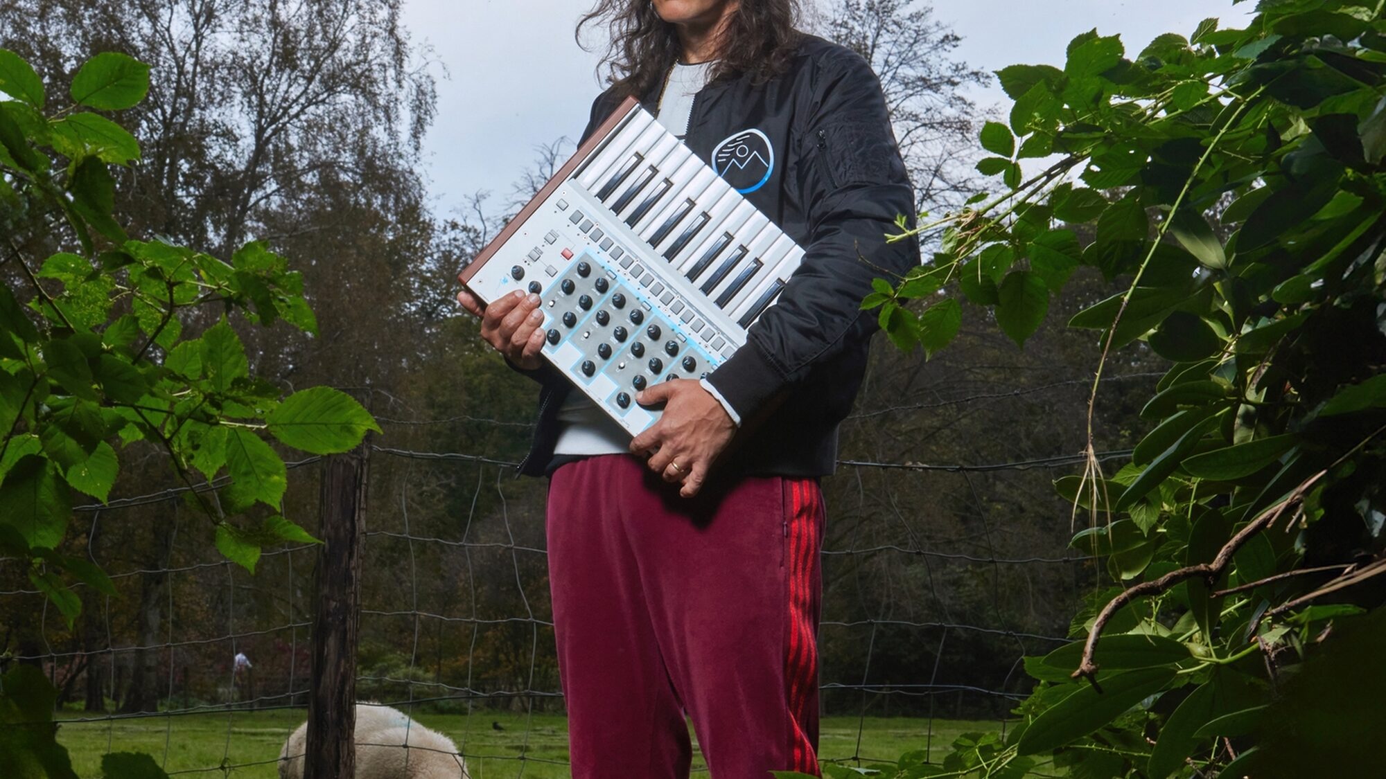 Electro-producer Legowelt in de natuur met een synthesizer onder zijn arm.