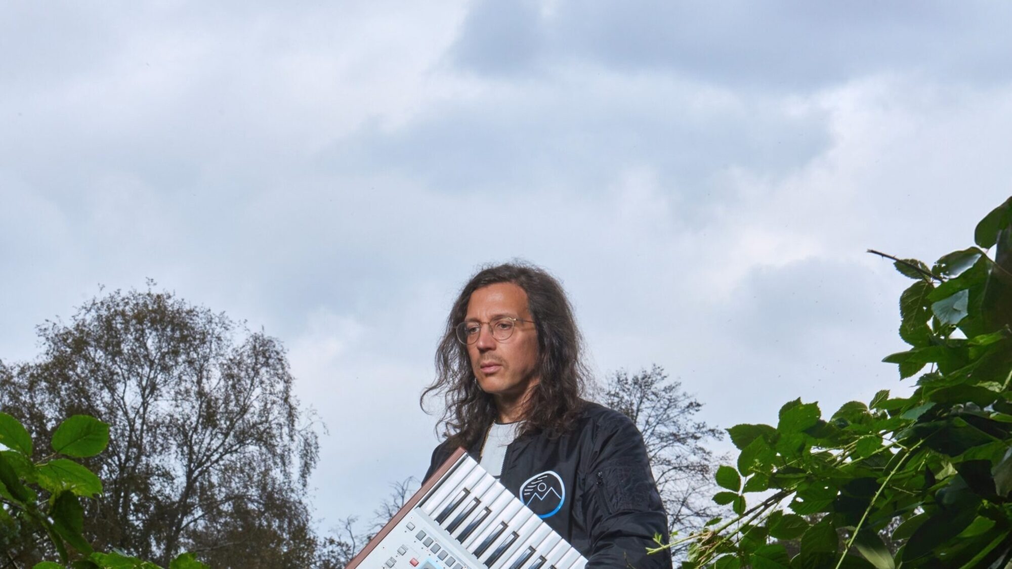 Electro-producer Legowelt in de natuur met een synthesizer onder zijn arm.